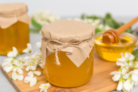 Sweet honey jar surrounded by spring acacia blossoms. Honey flows from a spoon in a jar. jars of...