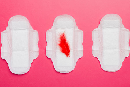 Women hygiene products or Sanitary pad with red feather on colored background. Pastel color....