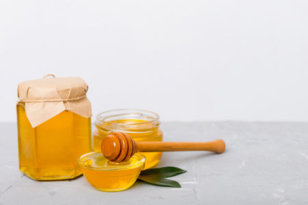 Honey in jar with leaves and honey dipper on colored background top view with copy text.