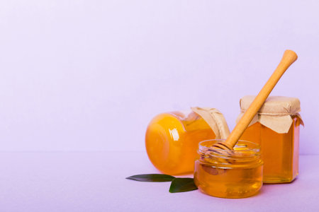 Honey in jar with leaves and honey dipper on colored background top view with copy text.の写真素材