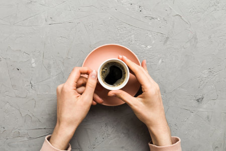 Minimalistic style woman hand holding a cup of coffee on colored background. Flat lay, top view cappuccino cup. Empty place for text, copy space. Top view, flat lay.の写真素材