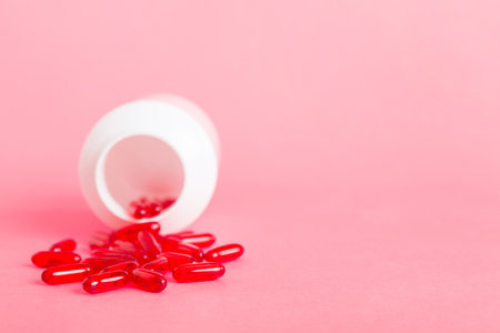 Red pills spilled around a pill bottle. Medicines and prescription pills flat lay background. Red medical capsules.の写真素材