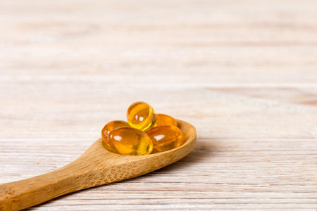 Vitamin omega capsules in a spoon on a colored background. Red soft gel vitamin supplement capsules on spoon.の写真素材