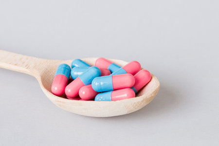 Vitamin capsules in a spoon on a colored background. Pills served as a healthy meal. Red soft gel...