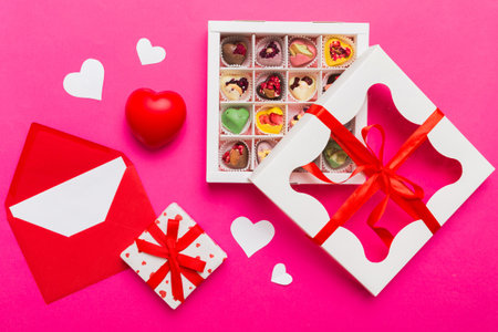 Red envelope with candy and gift box and Valentines hearts on colored background. Flat lay, top view. Romantic love letter for Holiday concept.の写真素材