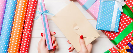 Top view of a woman holding an envelope in one hand and a small present in another on wooden background. New Year decorations. Christmas time concept.の写真素材