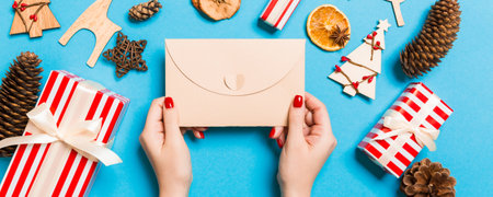 Top view of woman holding an envelope on blue background made of holiday decorations. Christmas time...