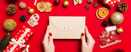 Top view of woman holding an envelope on red background made of holiday decorations. Christmas time concept.の写真素材
