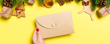 Top view of woman holding an envelope on yellow background made of holiday decorations. Christmas...