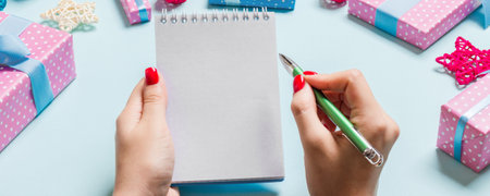 Top view of female hand making some notes in noteebok on blue background. New Year decorations and...