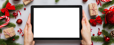 Christmas online shopping from home, female hands holding tablet pc with blank white display top view. woman hand holding tablet with blank screen, Christmas tree and gifts on background.の写真素材