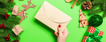 Top view of woman holding an envelope on green background made of holiday decorations. Christmas...