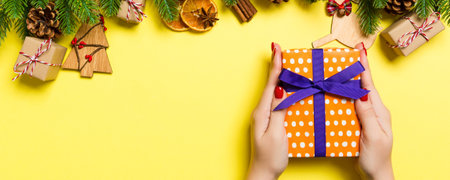 Top view of female hands holding a Christmas present on festive yellow background. Fir tree and holiday decorations. New Year holiday concept.の写真素材