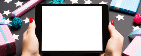 Top view of woman holding tablet in her hands on black background made of Christmas decorations. New...