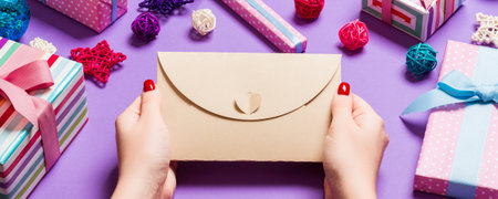 Top view of woman holding an envelope on purple background made of holiday decorations. Christmas...