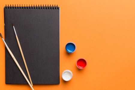 Album pages and paints, pencils, brushes on a colored background. Top view with empty space. workplace for creativity. home teaching concept drawing.の写真素材