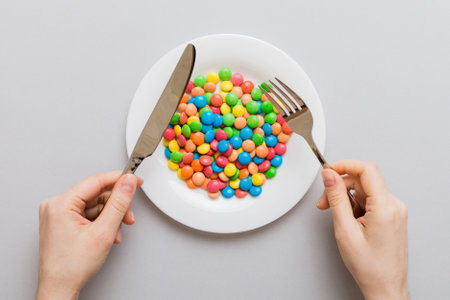 the girl holds cutlery in her hands and eats sweets in a plate. Top view on colored background.の写真素材