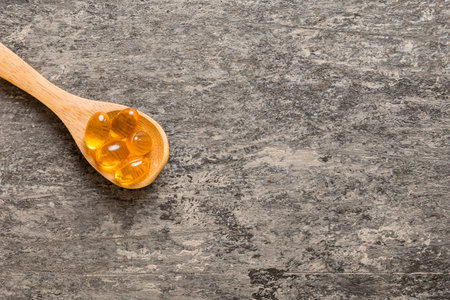 Vitamin omega capsules in a spoon on a colored background. Pills served as a healthy meal. Red soft gel vitamin supplement capsules on spoon.の写真素材