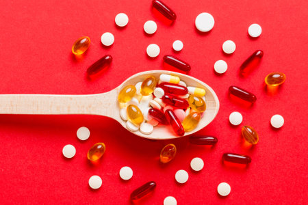 Vitamin capsules in a spoon on a colored background. Red soft gel vitamin supplement capsules on spoon.の写真素材