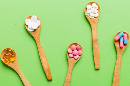 Vitamin capsules in a spoon on a colored background. Pills served as a meal. Red soft gel vitamin supplement capsules on spoon.の写真素材