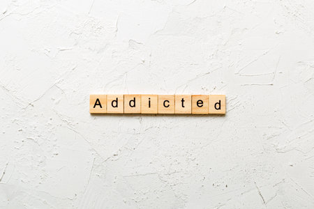 Addicted word written on wood block. Addicted text on cement table for your design, Top view concept.の写真素材