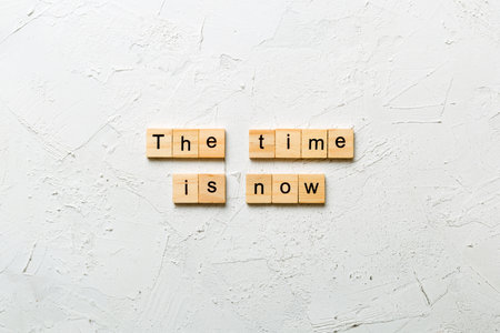 the time is now word written on wood block. the time is now text on table, concept.の写真素材