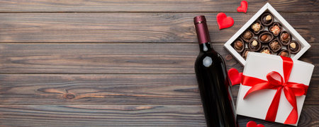 Bottle of red wine on colored background for Valentine Day with gift and chocolate. Heart shaped with gift box of chocolates top view with copy space.の写真素材