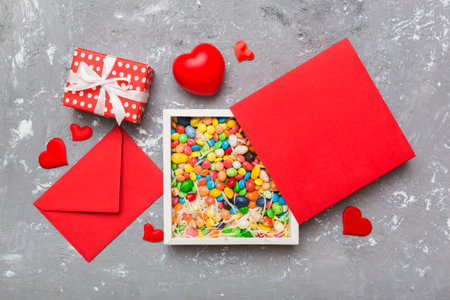 Red envelope with candy and gift box and Valentines hearts on colored background. Flat lay, top view. Romantic love letter for Holiday concept.の写真素材