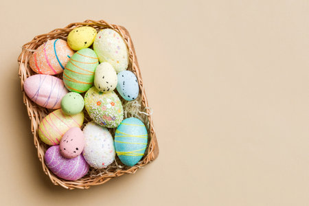 Colorful Easter eggs in wicker basket against colored background, closeup. top view with copy space.
