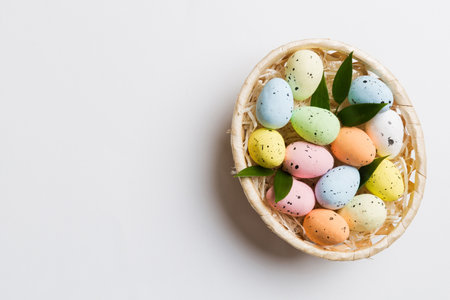 Colorful Easter eggs in wicker basket against colored background, closeup. top view with copy space.