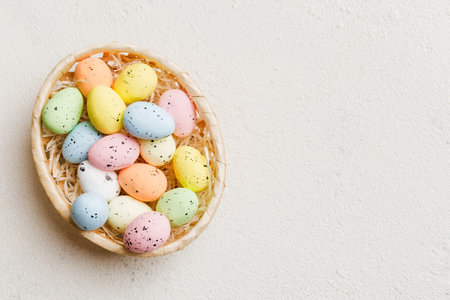 Colorful Easter eggs in wicker basket against colored background, closeup. top view with copy space.