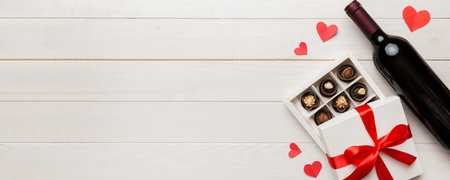 Bottle of red wine on colored background for Valentine Day with gift and chocolate. Heart shaped with gift box of chocolates top view with copy space.の写真素材