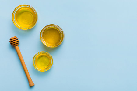 Glass jar of honey with wooden drizzler on colored background. Honey pot and dipper high above. Top view copy space.の写真素材