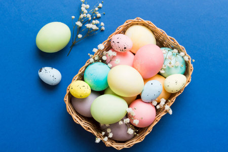 Happy Easter composition. Easter eggs in basket on colored table with gypsophila. Natural dyed colorful eggs background top view with copy space.の写真素材