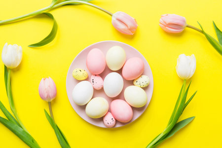 Happy Easter composition. Easter eggs in basket on colored table with yellow Tulips. Natural dyed colorful eggs background top view with copy space.の写真素材