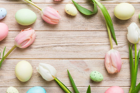 Happy Easter composition. Easter eggs on colored table with yellow Tulips. Natural dyed colorful eggs background top view with copy space.の写真素材