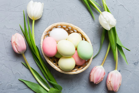 Happy Easter composition. Easter eggs in basket on colored table with yellow Tulips. Natural dyed colorful eggs background top view with copy space.の写真素材