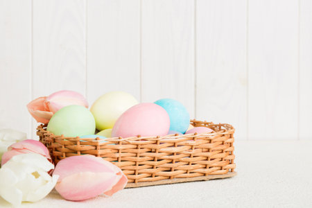 Happy Easter composition. Easter eggs in basket on colored table with yellow Tulips. Natural dyed colorful eggs background with copy space.の写真素材