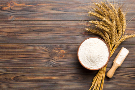 Flat lay of Wheat flour in wooden bowl with wheat spikelets on colored background.の写真素材