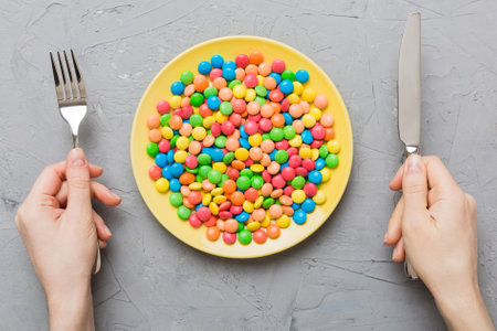 the girl holds cutlery in her hands and eats sweets in a plate. top view on colored background.の写真素材