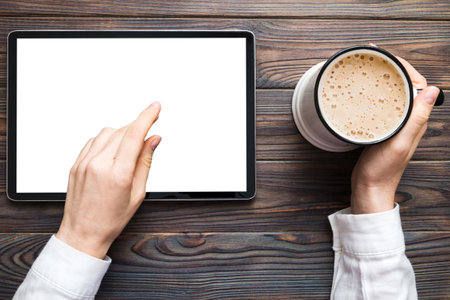 Close up image woman hands holding digital tablet with blank copy space screen for your text message or promotional content om table with cup of coffee. hands of a woman holding blank tablet device.の写真素材