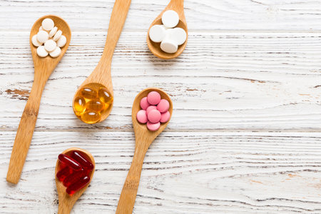 Vitamin capsules in a spoon on a colored background. Pills served as a healthy meal. Red soft gel vitamin supplement capsules on spoon.の写真素材