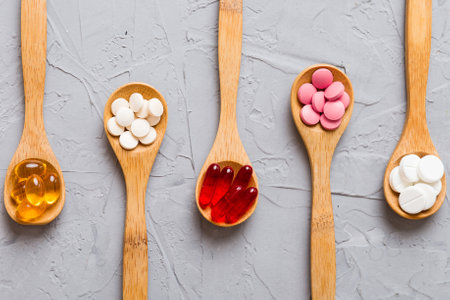 Vitamin capsules in a spoon on a colored background. Red soft gel vitamin supplement capsules on spoon.の写真素材