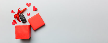 Black car key in a present box with a ribbon and red heart on colored background. Valentine day...