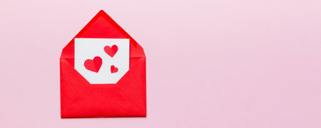 Red paper envelope with empty white card and heart on colored background. top view valentines day...