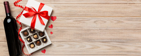 Bottle of red wine on colored background for Valentine Day with gift and chocolate. Heart shaped with gift box of chocolates top view with copy space.の写真素材
