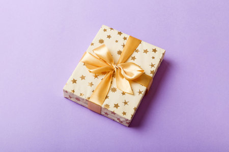 wrapped Christmas or other holiday handmade present in white paper with gold ribbon on colored background. Present box, decoration of gift on colored table, top view with copy space.の写真素材