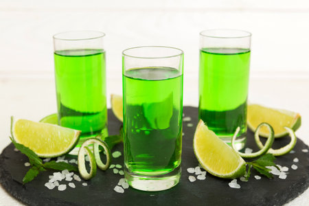 Sweet refreshing mint liqueur, with ice and mint leaves on table background, Shots with lime slice...