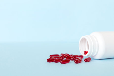 Red pills spilled around a pill bottle. Medicines and prescription pills flat lay background. Red...