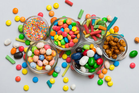 different colored round candy in bowl and jars. Top view of large variety of sweets and candies with...